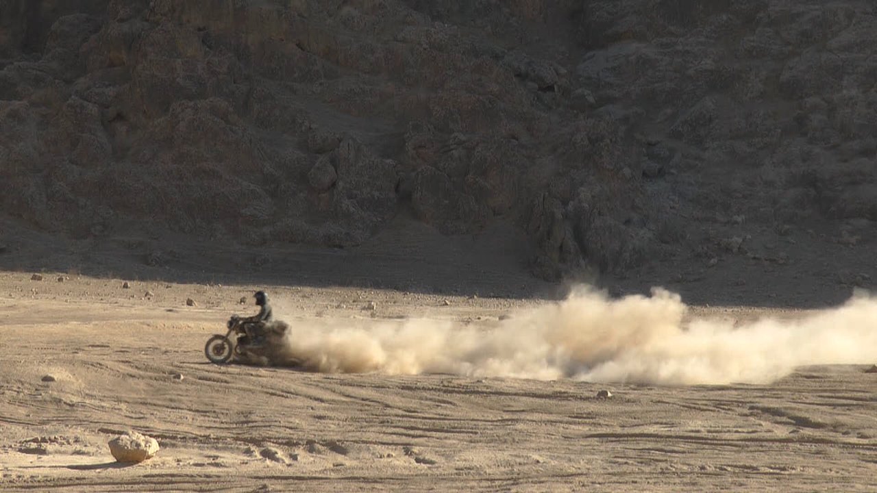 A motorcyclist kicking up a long cloud of dust in a rocky desert