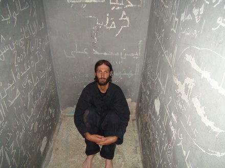 A man crouching in a prison cell covered in scratched Arabic writing