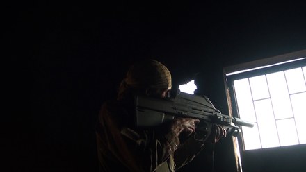A man aiming a rifle beside a bright window